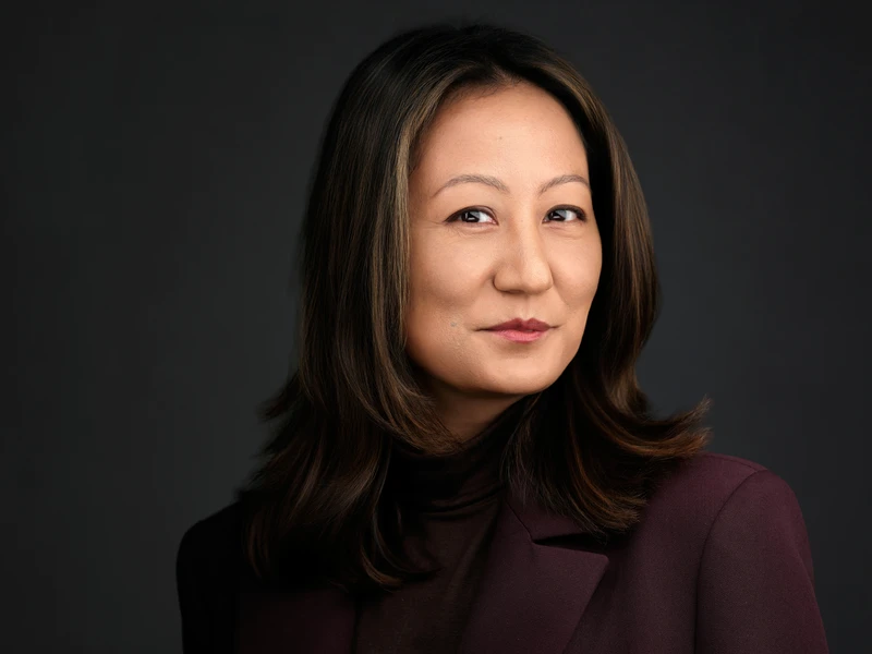 Professional headshot of a woman with dark hair in a burgundy blazer, composed confident expression