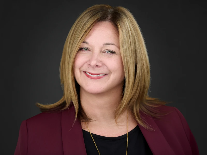 Professional headshot of a blonde woman in a burgundy blazer, warm natural smile