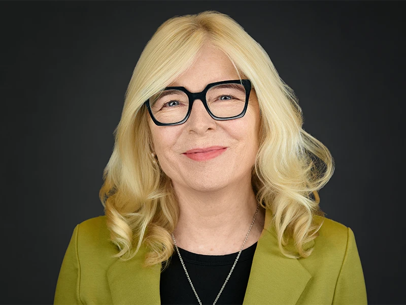 Woman in blazer and glasses, poised and professional, dark studio background
