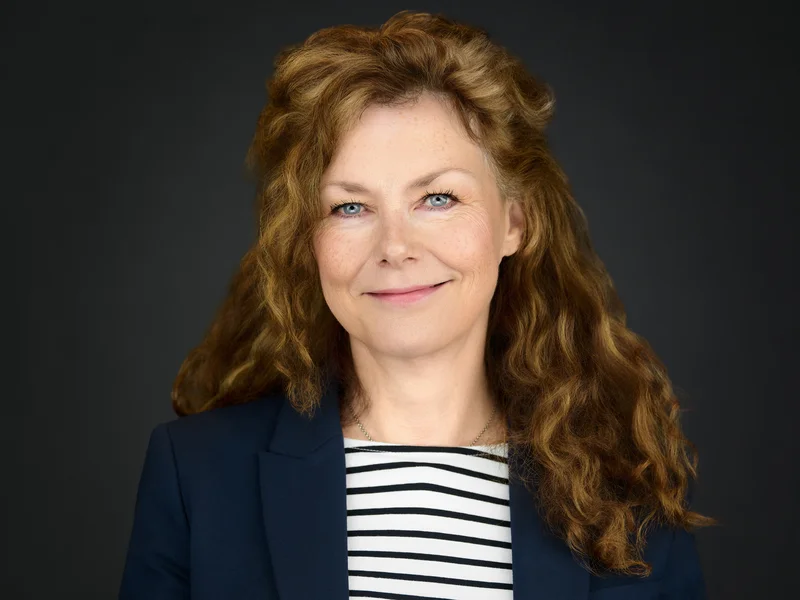Red-haired woman in a dark blazer, professional portrait with a calm and approachable expression