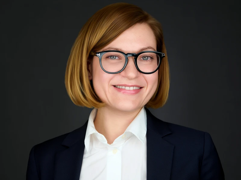 Professional headshot of a woman with a short bob and glasses in a dark blazer, warm friendly smile