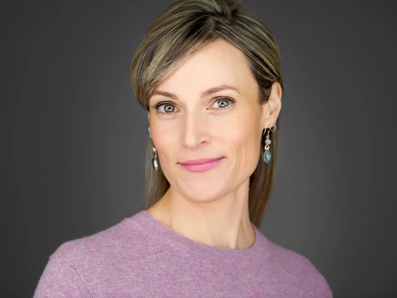 Headshot of a woman in a jumper on a dark studio background