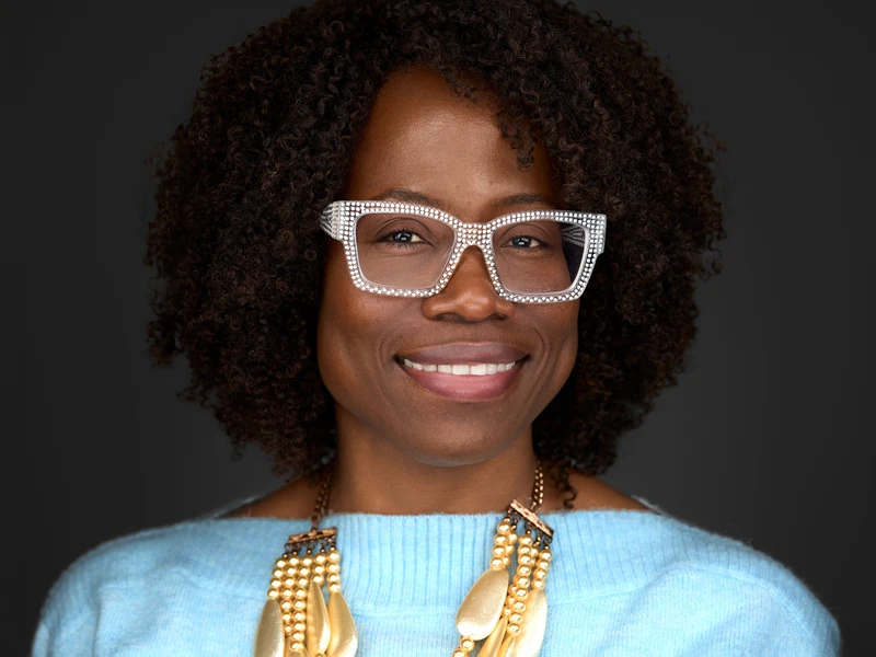 Woman in grey jumper and glasses, calm and confident expression, professional headshot on dark background
