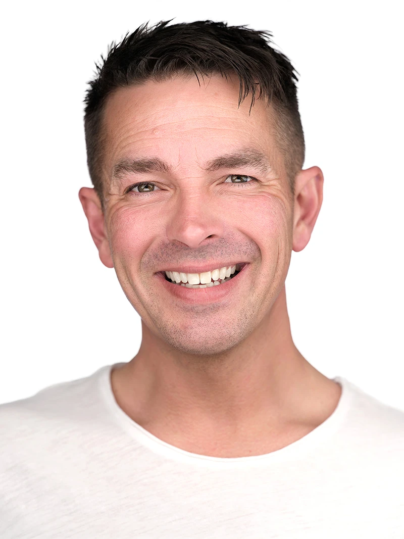 Corporate headshot on a clean white background, a smiling man in a white t-shirt, bright neutral studio lighting