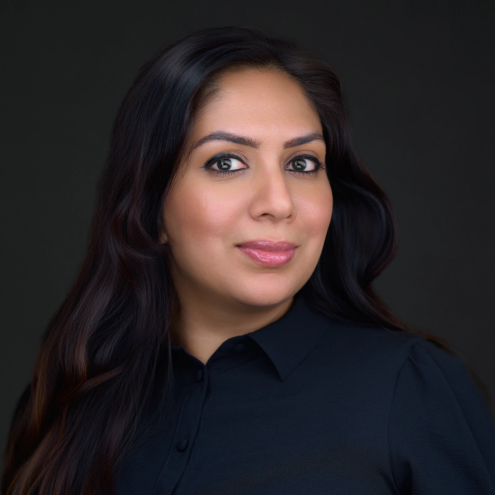 Professional headshot of a woman with long dark hair in a dark shirt, composed confident expression