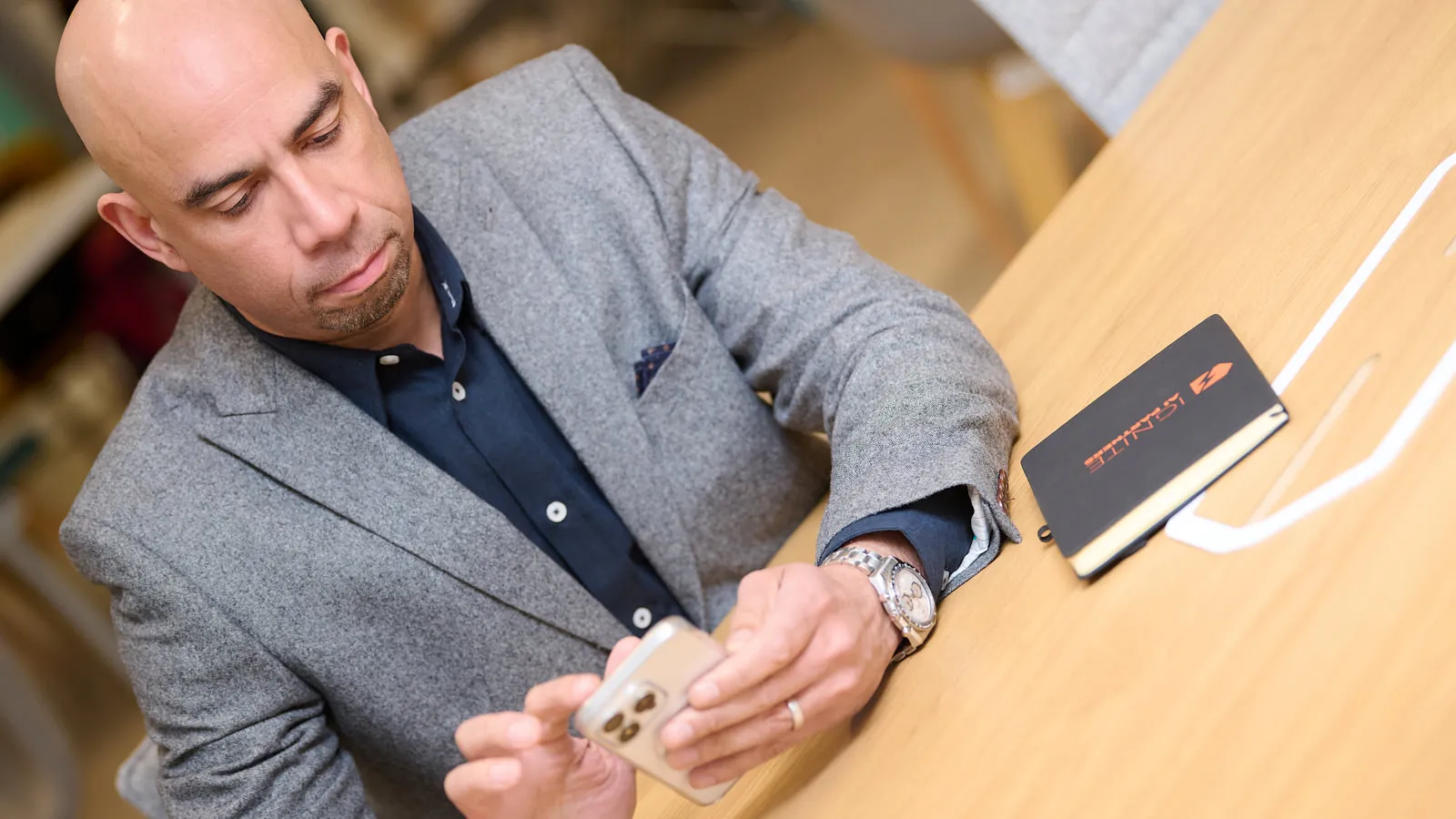 Overhead personal branding shot: man in a grey blazer checking his phone at a desk