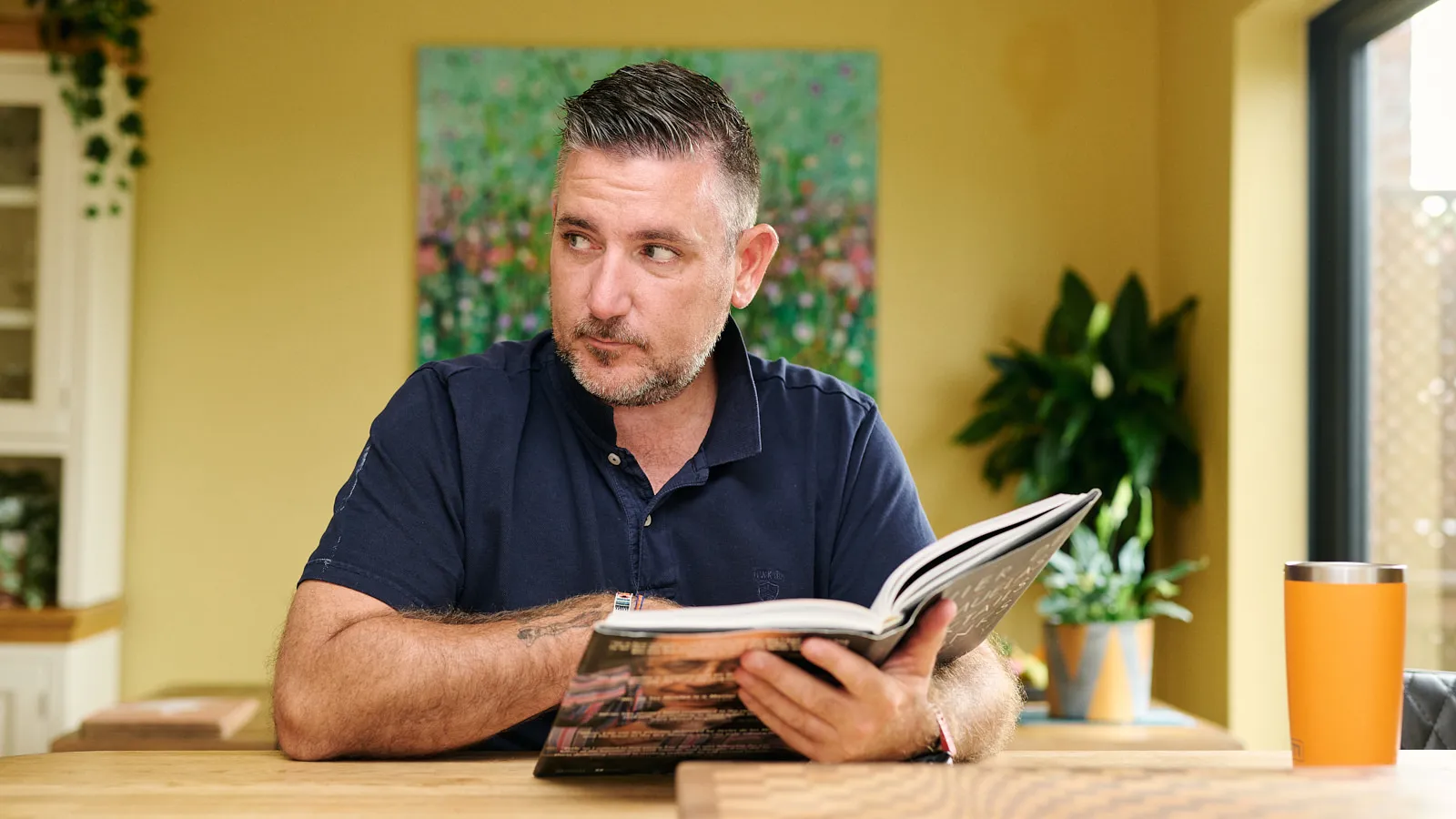 Man in a navy polo shirt reading at a kitchen table at home